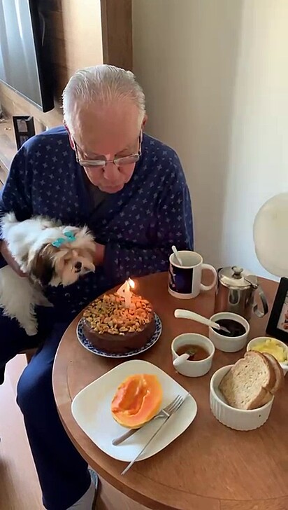 A Shih Tzu and her owner blowing out his birthday candle.